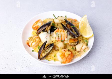 Risotto aux fruits de mer avec safran, persil et citron. Riz Arborio aux crevettes tigrées, aux moules et au calmar. Plats italiens traditionnels. Gros plan, foyer sélectif Banque D'Images