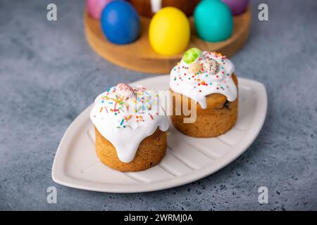 Deux petits kulichs de Pâques avec des fruits confits en glaçage blanc avec des saupoudrages colorés dans la coupe. Oeufs de poulet et de caille peints. Bak traditionnel de Pâques Banque D'Images