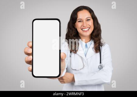 Offre de télémédecine. Jeune femme médecin montrant smartphone avec écran blanc blanc blanc, présentant une maquette pour l'application ou l'annonce Banque D'Images