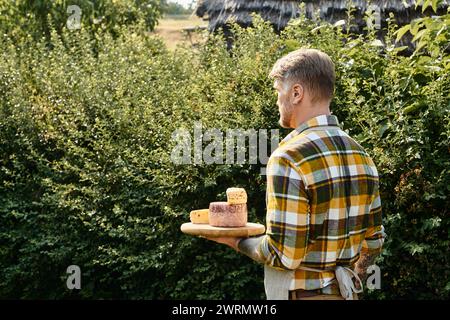 bon homme regardant avec des tatouages sur les bras dans une tenue décontractée tenant du fromage et regardant loin pendant à la ferme Banque D'Images