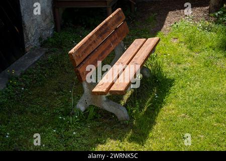 Banc en bois sur une herbe printanière vert vif. Journée ensoleillée. Situé dans un parc au cimetière d'une église All Saint. Dlouhomilov, Moravie, république tchèque Banque D'Images