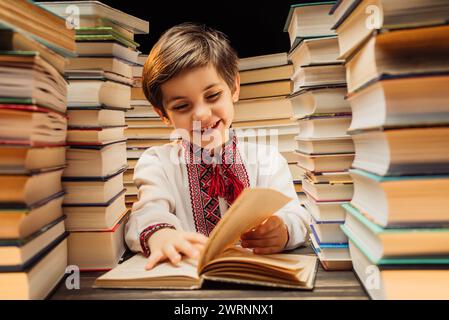 Beau petit enfant ukrainien feuillette les pages de livre dans la bibliothèque. Garçon d'école primaire appréciant la lecture dans la librairie ou la librairie Banque D'Images