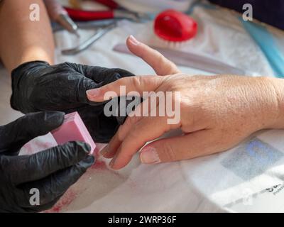 Manucure femme à l'aide d'une éponge de polissage après avoir enlevé le vieux vernis pour la peinture permanente des ongles Banque D'Images