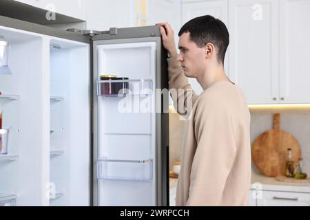 Homme bouleversé près d'un réfrigérateur vide dans la cuisine Banque D'Images