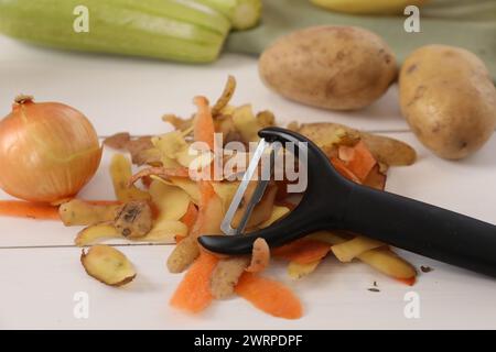 Pelures de légumes frais et éplucheur sur la table en bois blanc, gros plan Banque D'Images