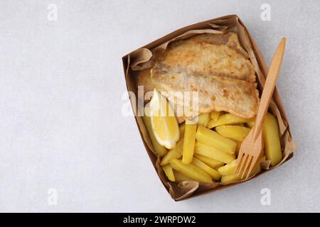 Délicieux poisson et frites dans une boîte en papier servie sur une table gris clair, vue de dessus. Espace pour le texte Banque D'Images