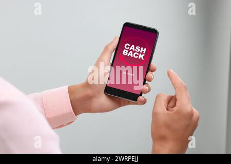 Homme utilisant un smartphone avec le mot Cashback sur fond flou, gros plan Banque D'Images