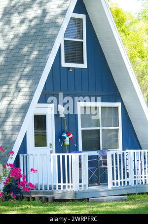 Gros plan de mignon Adorable Une maison en forme de triangle de cadre ou maison avec la couleur bleu foncé, toit de bardeaux gris, porte blanche, garde-corps de porche en bois, rose re Banque D'Images