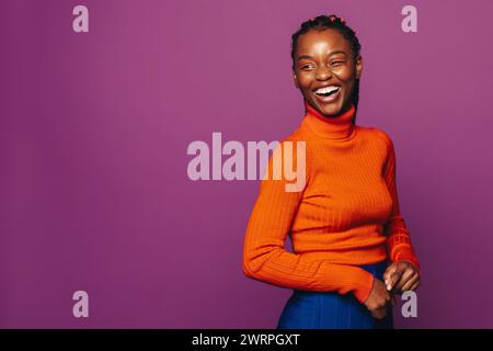 Jeune femme heureuse dans la vingtaine se tient dans un studio, portant des vêtements décontractés et un col polo violet éclatant. Ses élégantes tresses bicolores mettent en valeur son fashi Banque D'Images