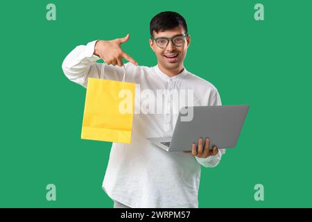 Beau jeune homme avec sac à provisions et ordinateur portable sur fond vert Banque D'Images
