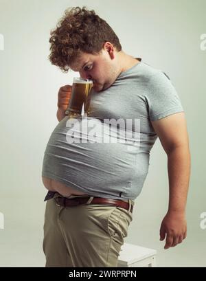 Obèse, gain de poids et alcool pour homme en studio avec boisson pour habitude malsaine, plus la taille et la blague. Personne en surpoids avec verre sur l'estomac gras pour Banque D'Images