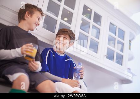 Cuisine, équipe et garçons avec le sourire pour les boissons, le football ou le football et la pratique pour le match avec le ballon. Amis, enfants et enfants prêts dans la maison pour Banque D'Images