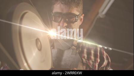 Image d'une lumière incandescente au-dessus d'un homme caucasien travaillant dans un atelier Banque D'Images