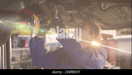 Image d'une lumière incandescente au-dessus d'une femme caucasienne mécanicienne automobile dans un atelier Banque D'Images