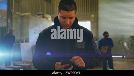 Image de la lumière incandescente sur l'homme caucasien à l'aide d'un smartphone travaillant en usine Banque D'Images