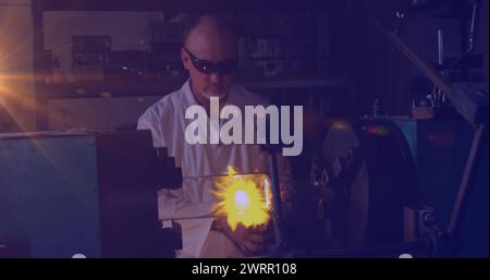 Image d'une lumière incandescente au-dessus d'un homme caucasien travaillant dans un atelier Banque D'Images