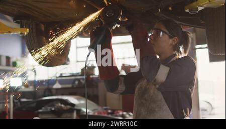 Image d'une lumière incandescente au-dessus d'une femme caucasienne mécanicienne travaillant dans un atelier Banque D'Images