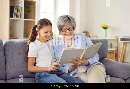 Grand-mère lisant un livre à sa petite-fille fille assise au canapé à la maison. Banque D'Images