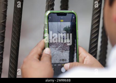 Mexico, Mexique. 13 mars 2024. Les passants prennent des photos et observent une réplique d'une colossale tête olmèque écrasant une voiture Tesla dans un terrain vacant à Mexico. L'intervention est attribuée au sculpteur Chavis Marmol, originaire d'Apan, Hidalgo, et il affirme que cette action ''vise à explorer des réflexions sur des questions contemporaines à travers son mélange d'humour et de critique''. L'œuvre est intitulée Neo-Ta meme, qui ''aborde le passé préhispanique du Mexique d'un point de vue néo-colonial occidental''. (Photo de Gerardo Vieyra/NurPhoto)0 crédit : NurPhoto SRL/Alamy Live News Banque D'Images