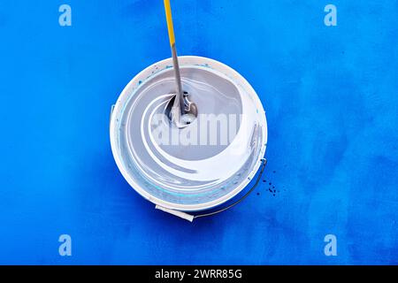 Teindre et mélanger la peinture avec la tige d'agitation ou le mélangeur pour les peintures, peintre de maison a ajouté le pigment de toner au seau, fond bleu. Banque D'Images