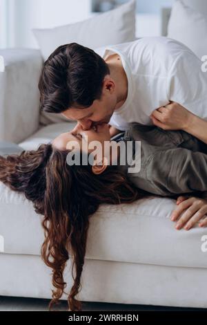 Un homme embrasse doucement son partenaire , capturant un moment tendre et affectueux entre eux alors qu'ils se détendent sur un canapé. Leur proximité dépeint un lien profond et une affection. Couple intime profitant d'un moment tendre Banque D'Images