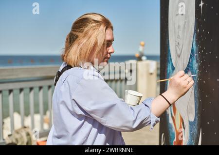 Jeune peintre féminine peint passionnément image avec pinceau pour l'exposition de rue en plein air, artiste féminine engrossée dans la création d'œuvres d'art vibrantes à Banque D'Images