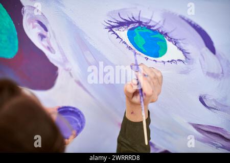 Peintre féminin dessine l'image avec un pinceau sur la toile pour l'exposition de rue extérieure, gros plan au-dessus de la vue de dessus de l'artiste féminin appliquer des coups de pinceau à c. Banque D'Images