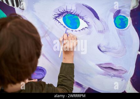 Peintre féminin dessine l'image avec un pinceau sur la toile pour l'exposition de rue extérieure, gros plan au-dessus de la vue de dessus de l'artiste féminin appliquer des coups de pinceau à c. Banque D'Images