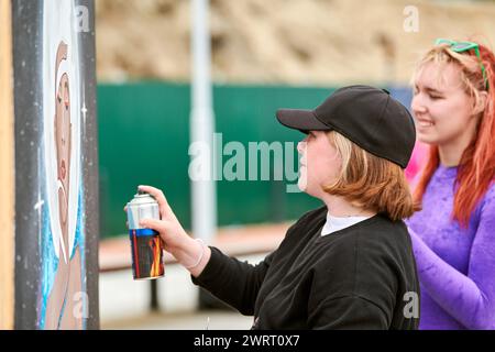 Deux artistes féminins peignant le tableau avec le spray de peinture peuvent le pulvériser sur la toile à l'exposition de rue extérieure, vue de côté de la passionnée femme art make Banque D'Images