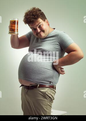 Obèse, gain de poids et bière pour homme en studio avec de l'alcool pour les habitudes malsaines, plus la taille et l'humour. Personne en surpoids avec verre à la main et graisse Banque D'Images