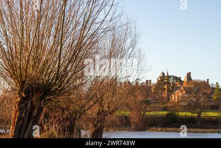 Par le Framlingham Mere ou lac pollarded arbres au premier plan et la lumière du soleil d'hiver avec la pile gothique qui est Fram College au milieu Banque D'Images