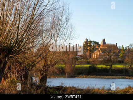 Par le Framlingham Mere ou lac pollarded arbres au premier plan et la lumière du soleil d'hiver avec la pile gothique qui est Fram College au milieu Banque D'Images