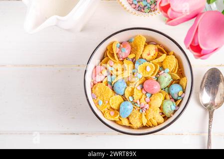 Céréales de petit-déjeuner de Pâques, flocons de maïs avec des œufs de chocolat de Pâques et des saupoudres de sucre, verser du lait ou du yaourt dans la portion de céréales de petit-déjeuner dorées de maïs Banque D'Images