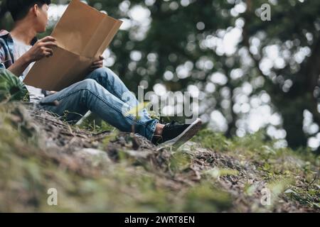 Randonneur perdu avec sac à dos assis près de la rivière et vérifie la carte pour trouver des directions dans la forêt. concept de randonnée et d'aventure. Banque D'Images