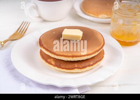 Pile de crêpes de petit déjeuner maison fraîchement cuites avec beurre et miel ou sirop d'érable sur une table en bois blanc Banque D'Images