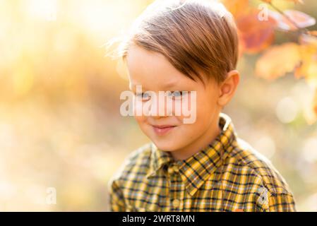 Portrait d'automne d'un petit garçon souriant aux cheveux clairs dans une chemise jaune dans le parc Banque D'Images