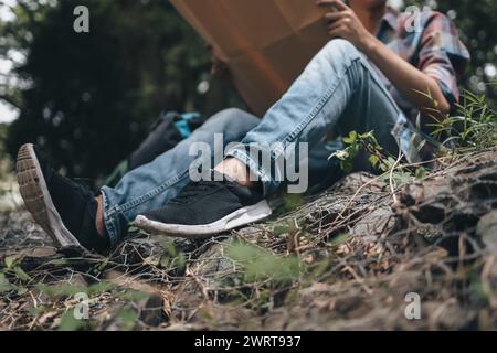 Randonneur perdu avec sac à dos assis près de la rivière et vérifie la carte pour trouver des directions dans la forêt. concept de randonnée et d'aventure. Banque D'Images