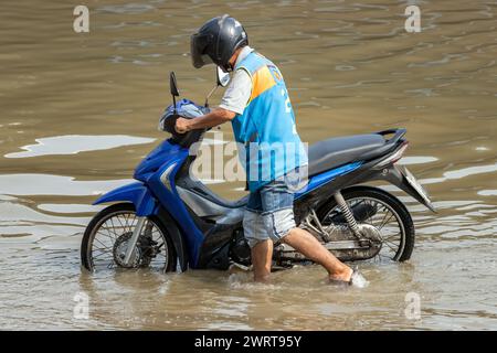 Un chauffeur de moto-taxi pousse une moto dans une rue inondée, en Thaïlande Banque D'Images