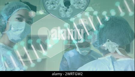 Image d'un brin d'ADN tournant et d'icônes médicales sur des chirurgiens portant des masques pendant un opérat Banque D'Images