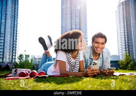 Photo pleine longueur de deux belles personnes joyeuses posant une couverture tenir un téléphone intelligent passer du temps libre l'air frais à l'extérieur Banque D'Images