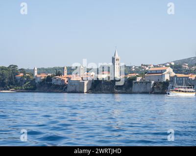 Bateau d'excursion en face de la ville de Rab dans la lumière du matin, tours d'église vues de la mer, Rab, île de Rab, baie du golfe de Kvarner, Croatie Banque D'Images