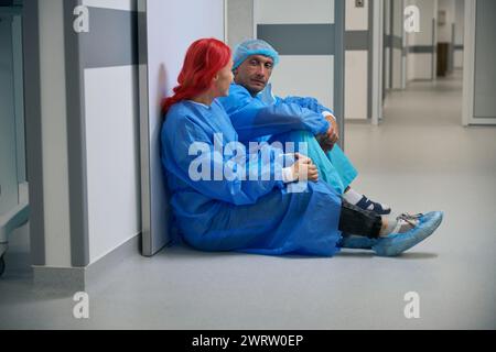 Les médecins assis dans le couloir fatigués après l'opération après de longues heures de travail Banque D'Images
