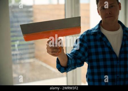 Gros plan d'un ouvrier debout dans la pièce et tenant la spatule à la main Banque D'Images