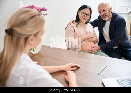 Couple de famille adulte visitant le bureau obstétricien pour parler du troisième trimestre de la grossesse et le processus de l'accouchement de bébé avec son aide, enfant contractuel Banque D'Images