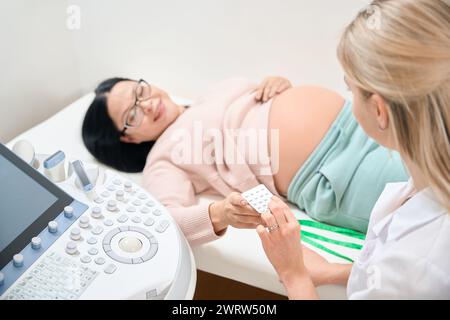 Gynécologue féminin prescrivant des pilules à la femme enceinte pour soutenir son niveau de calcium et de minéraux dans l'organisme pendant la grossesse, l'hormonothérapie, la guérison Banque D'Images