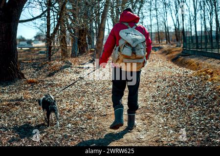 un homme avec un sac à dos marche avec un chien le long d'une allée de parc Banque D'Images