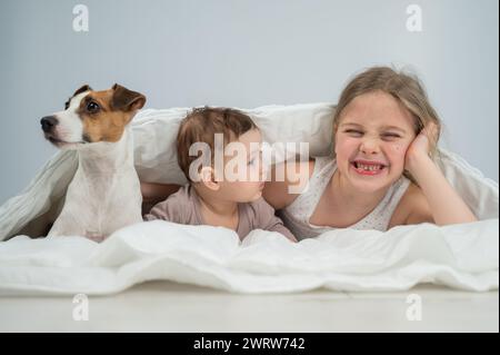 Une petite fille, son frère de cinq mois et le chien Jack Russell Terrier sont enveloppés dans une couverture. Banque D'Images