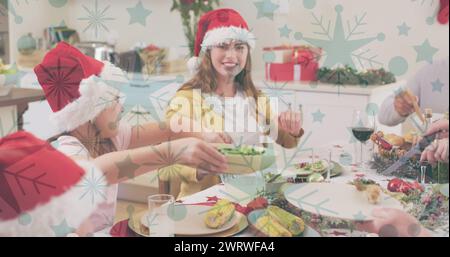 Image de neige tombant sur une famille caucasienne souriante avec des chapeaux de père noël dînant Banque D'Images