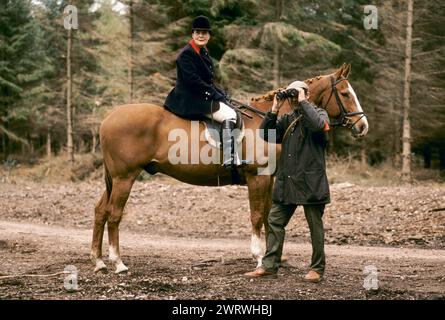 Quantock Hills, Somerset, Angleterre vers mars 1997. Les Quantock Staghounds, une dame chasse-femme et un suiveur de pied utilisant une paire de jumelles pour voir s'il peut apercevoir le cerf dans le bois. ANNÉES 1990 ROYAUME-UNI HOMER SYKES Banque D'Images