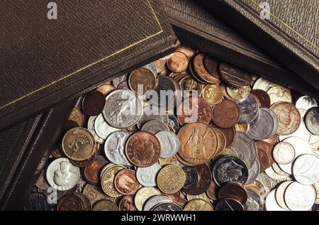 Photo de vieux livres anciens posés sur une pile dispersée de pièces de monnaie du monde. Vue supérieure de la table. Banque D'Images